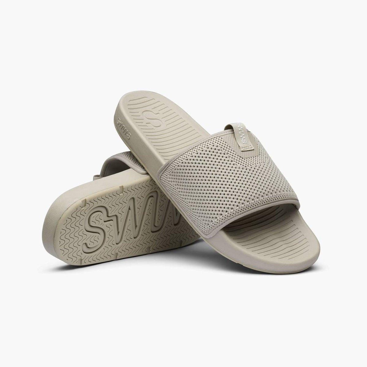 A pair of light gray slide sandals with a perforated mesh upper strap, shown from a three-quarters angle on a light gray background. SWIMS Slides available at Sakks Menswear in Southampton.