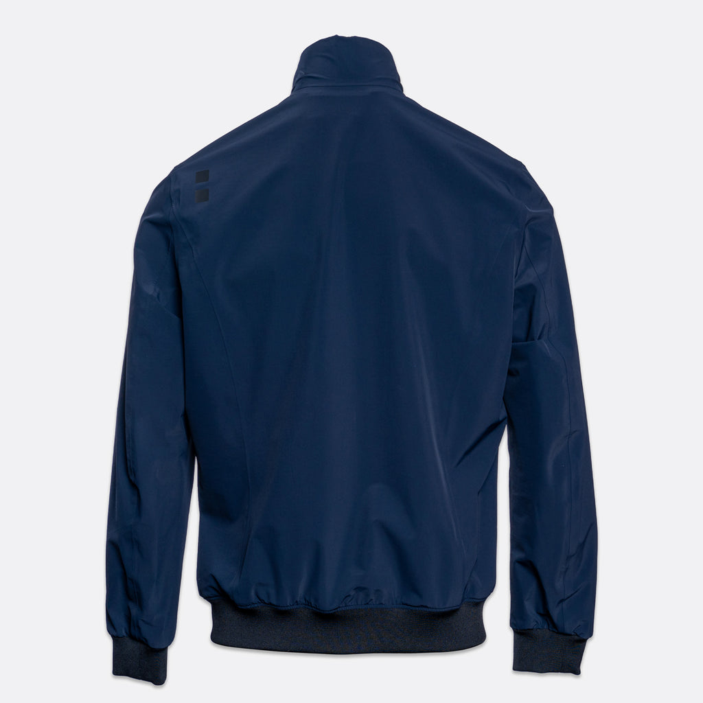 A navy blue lightweight jacket shown from the back, featuring a stand-up collar, ribbed cuffs, and a ribbed hem, photographed against a light gray background. UBR Jacket available at Sakks Menswear in Southampton.