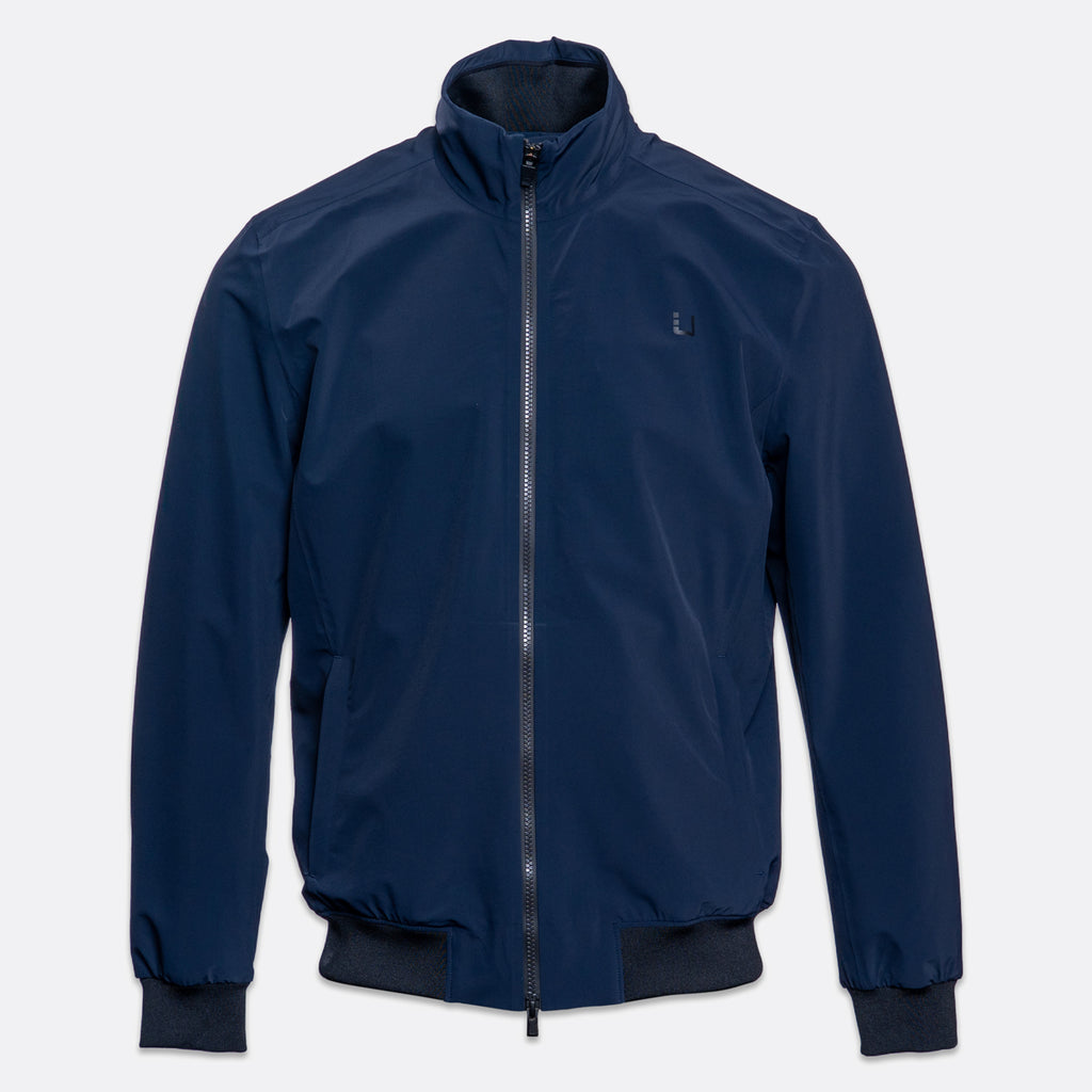 A navy blue lightweight zip-up jacket with a stand-up collar, ribbed cuffs, and a ribbed hem, shown against a light gray background. UBR Jacket available at Sakks Menswear in Southampton.