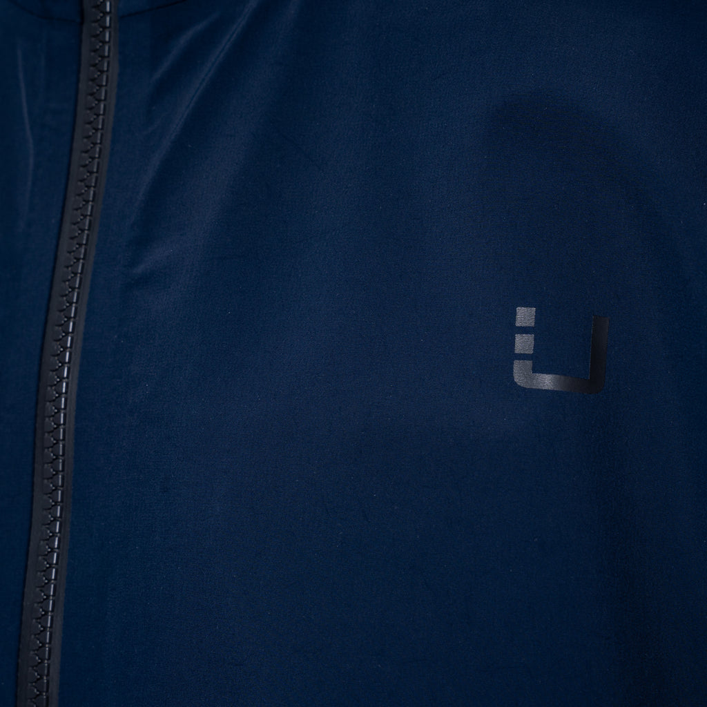 Close-up of a dark navy blue jacket with a black zipper on the left and a small dark gray stylized 'U' logo on the chest. UBR Jacket available at Sakks Menswear in Southampton.