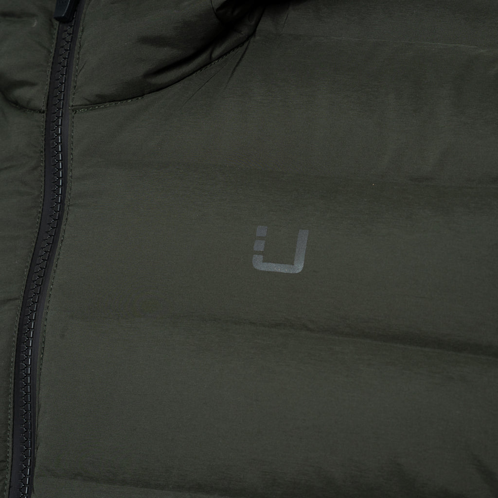 Close-up of an olive green puffer jacket with a dark zipper and a small gray stylized logo on the chest. UBR Jacket available at Sakks Menswear in Southampton.
