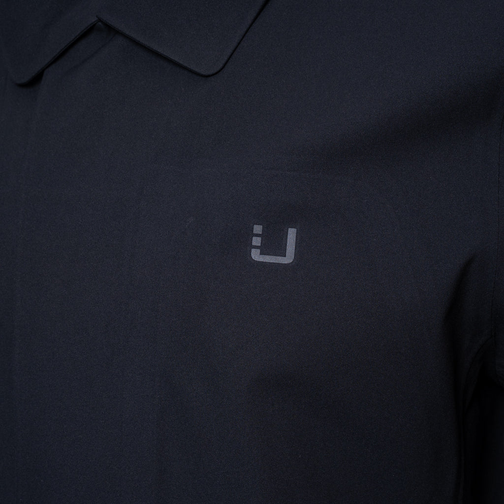 Close-up of a dark navy polo shirt with a small light gray embroidered logo on the chest. UBR Jacket available at Sakks Menswear in Southampton.