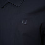 Close-up of a dark navy polo shirt with a small light gray embroidered logo on the chest. UBR Jacket available at Sakks Menswear in Southampton.