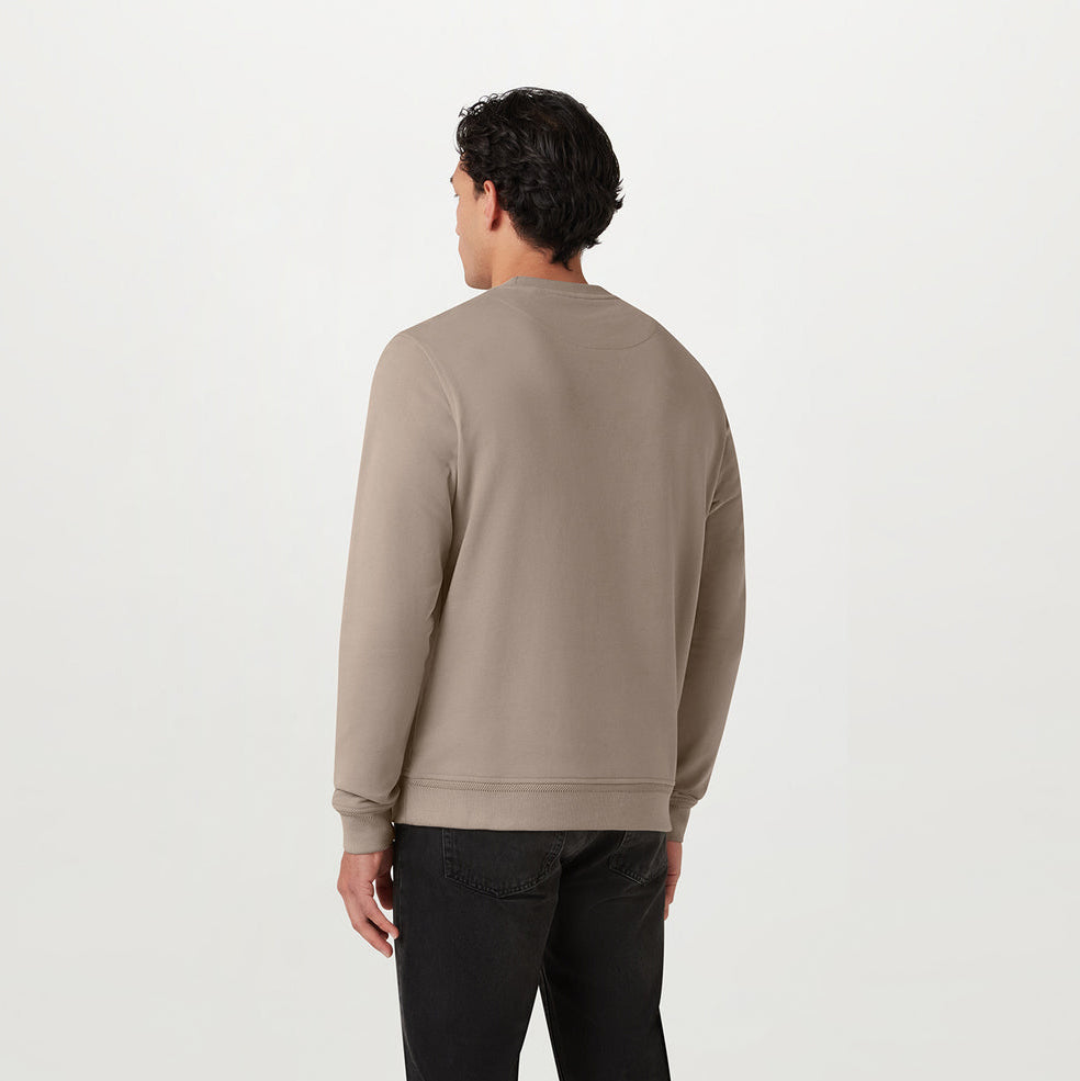 A man stood facing away in a beige coloured Belstaff Sweatshirt. The model is stood in front of a grey background. Belstaff Sweatshirt. Sakks Menswear Southampton.