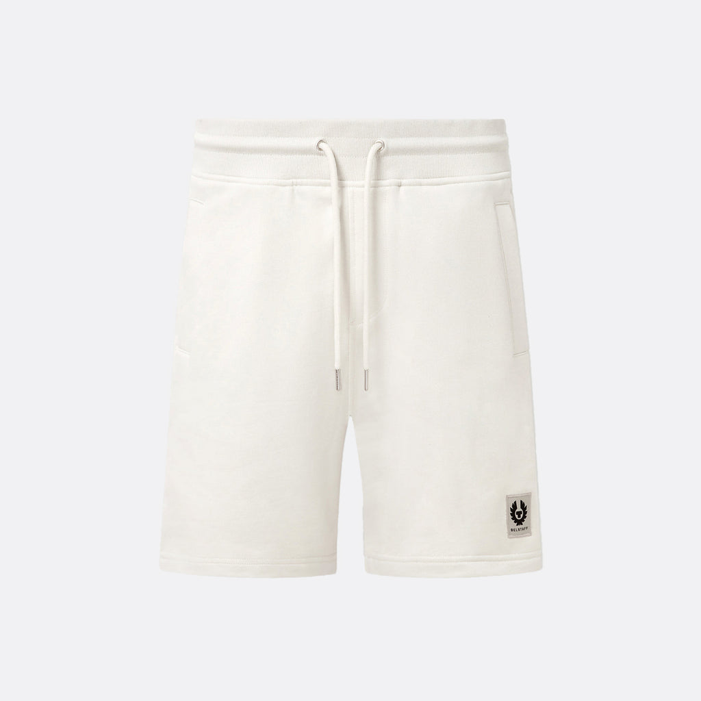Off-white fleece drawstring shorts with a small black logo patch on the lower left leg, shown against a light gray background. Belstaff Sweatshorts. Sakks Menswear Southampton.