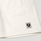 Close-up of an off-white cotton garment, likely a sweatshirt or jacket, showing a small square Belstaff logo patch on the lower right side. Belstaff Sweatshorts. Sakks Menswear Southampton.