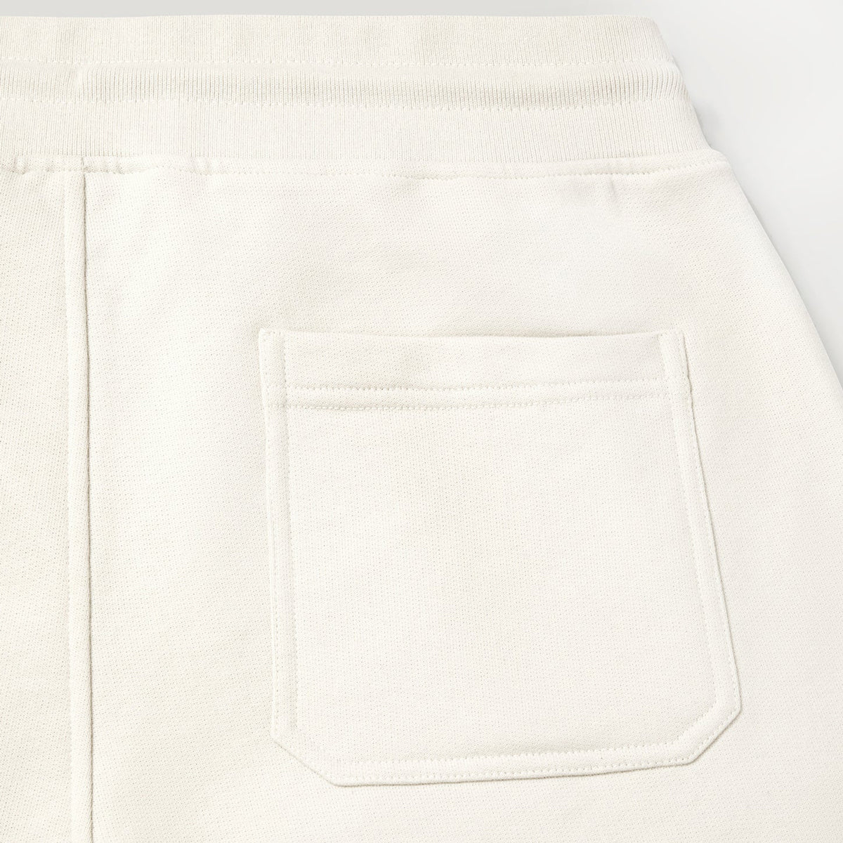 Close-up of a white or off-white fabric garment showing a rectangular front patch pocket and a ribbed waistband. Belstaff Sweatshorts. Sakks Menswear Southampton.